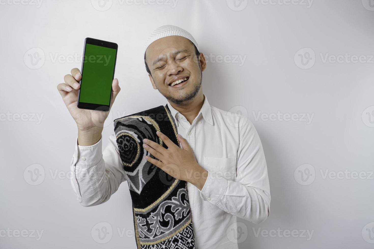 ritratto di un' tranquillo, calmo asiatico musulmano uomo è mostrando copia spazio su il suo Telefono e sorridente sentire sollievo foto