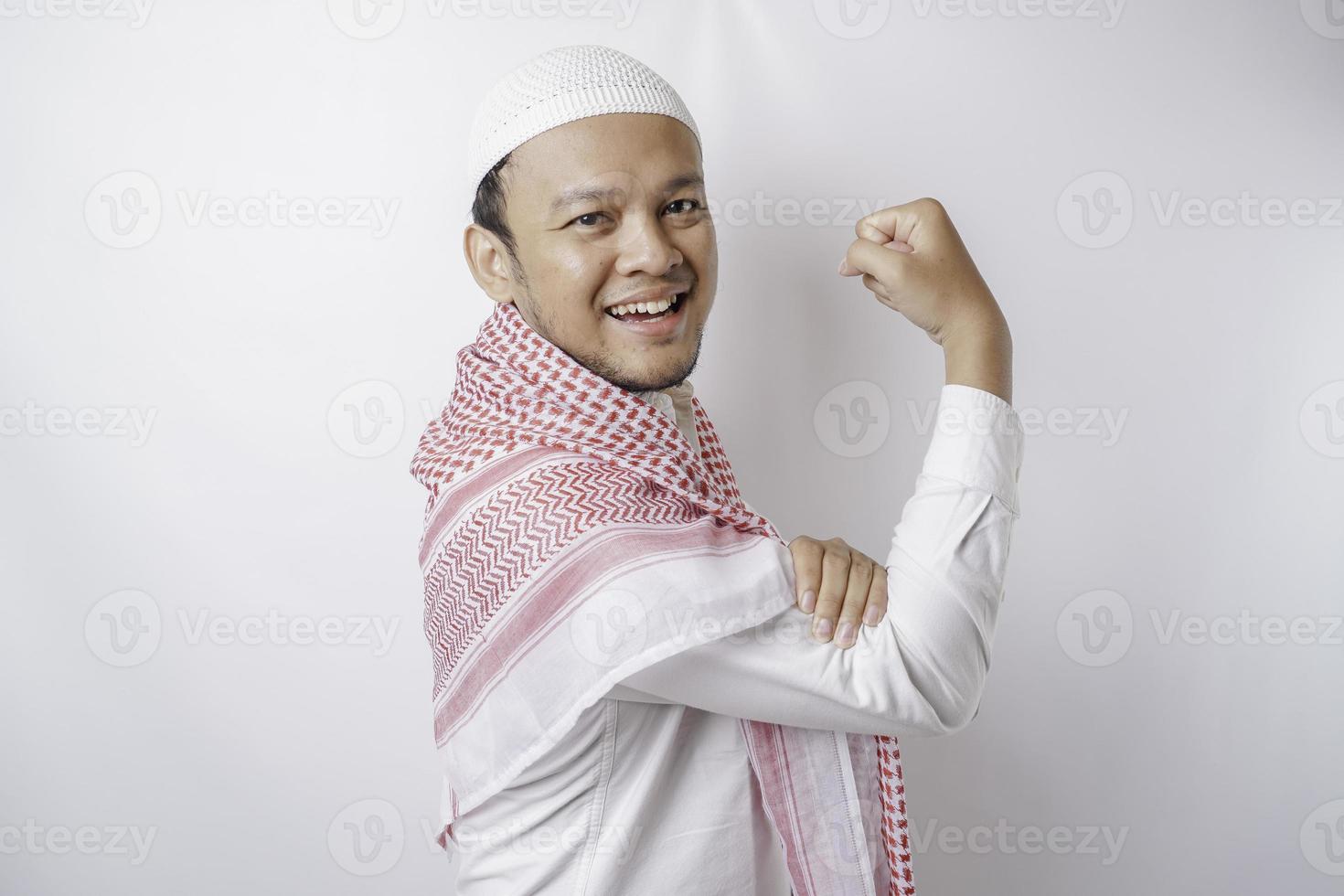 eccitato asiatico musulmano uomo mostrando forte gesto di sollevamento il suo braccia e muscoli sorridente con orgoglio foto