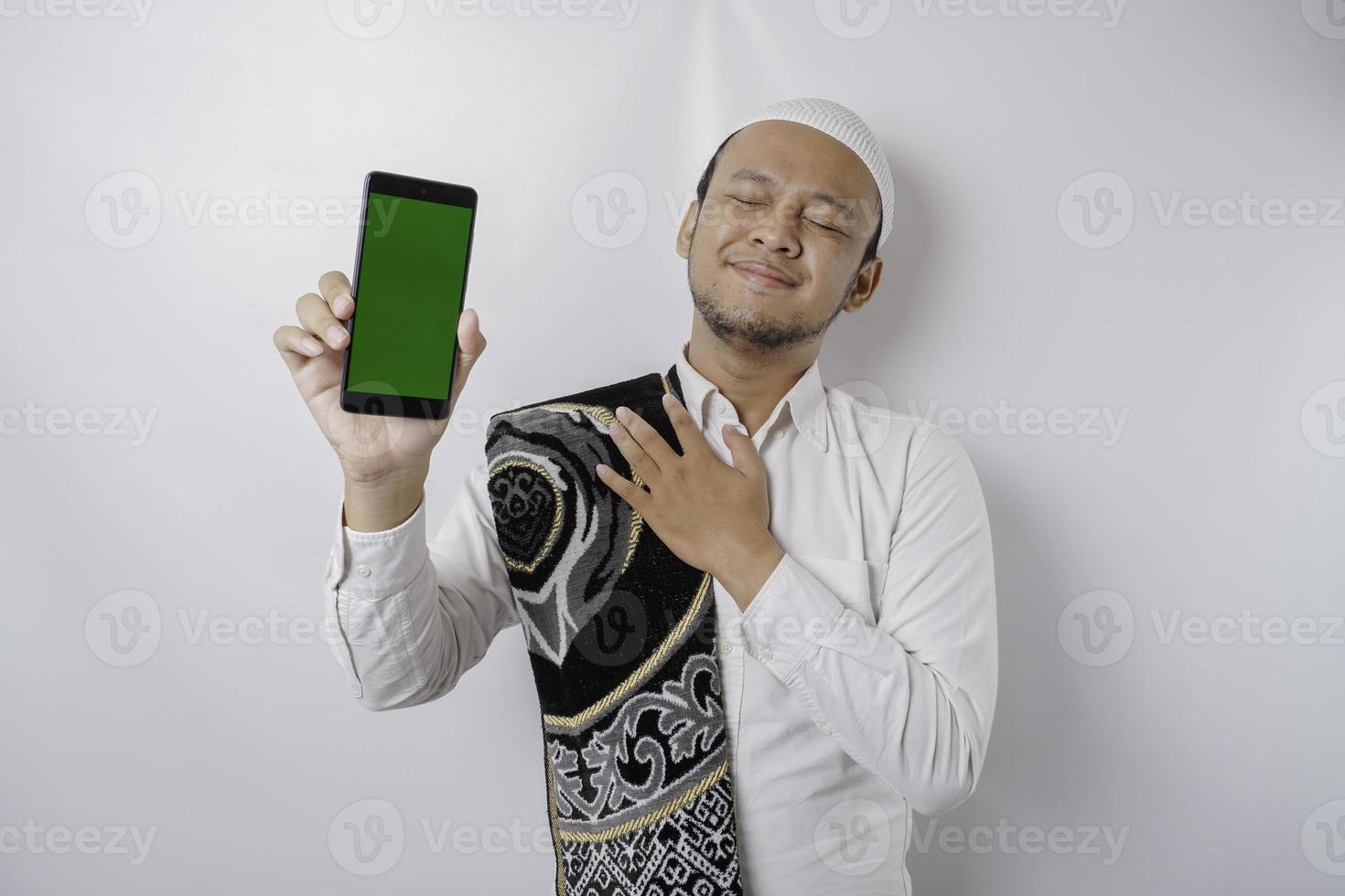 ritratto di un' tranquillo, calmo asiatico musulmano uomo è mostrando copia spazio su il suo Telefono e sorridente sentire sollievo foto