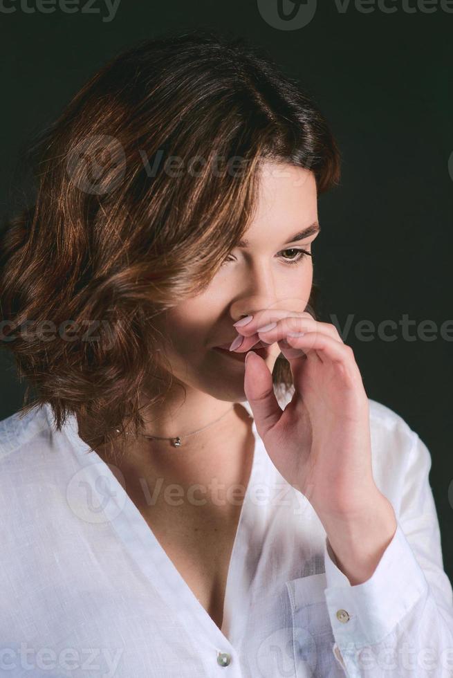 ritratto di giovane, bellissimo triste attrice con corto Marrone capelli nel bianca camicia e blu pantaloni nel il studio foto