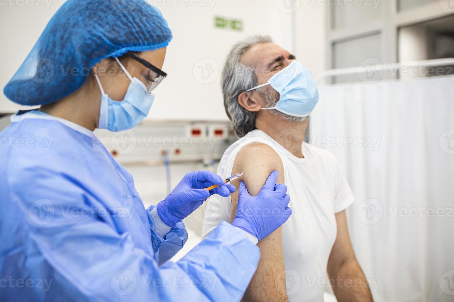 vicino su di generale professionista mano Tenere vaccino iniezione mentre indossare viso protettivo maschera durante covid-19 pandemia. giovane donna infermiera con chirurgico maschera dando iniezione per anziano uomo. foto