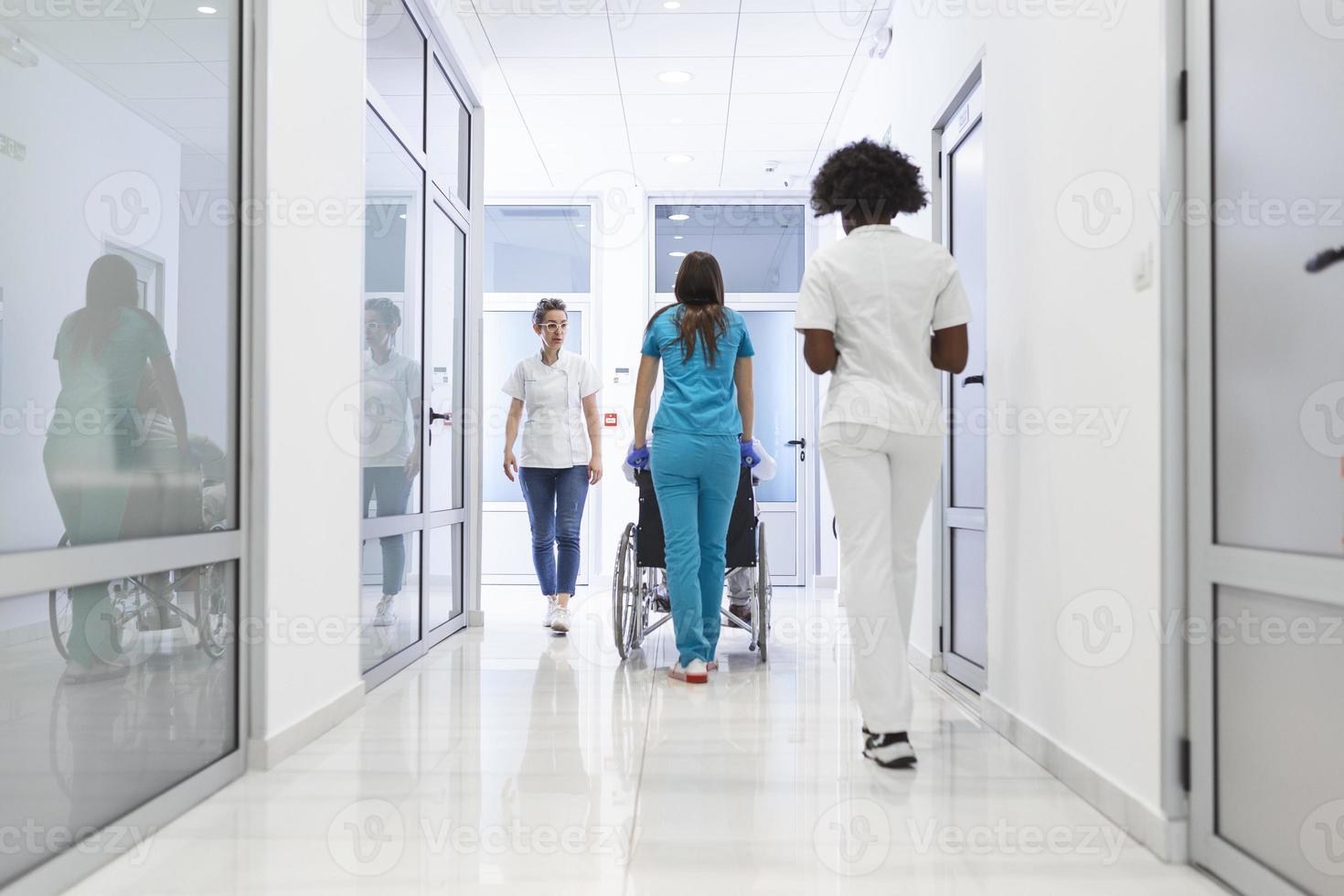 primo pavimento di il occupato Ospedale, medici, infermieri e personale occupato Lavorando, assistente si sposta anziano uomo nel il sedia a rotelle. nuovo moderno medico ospedale con professionale personale. foto