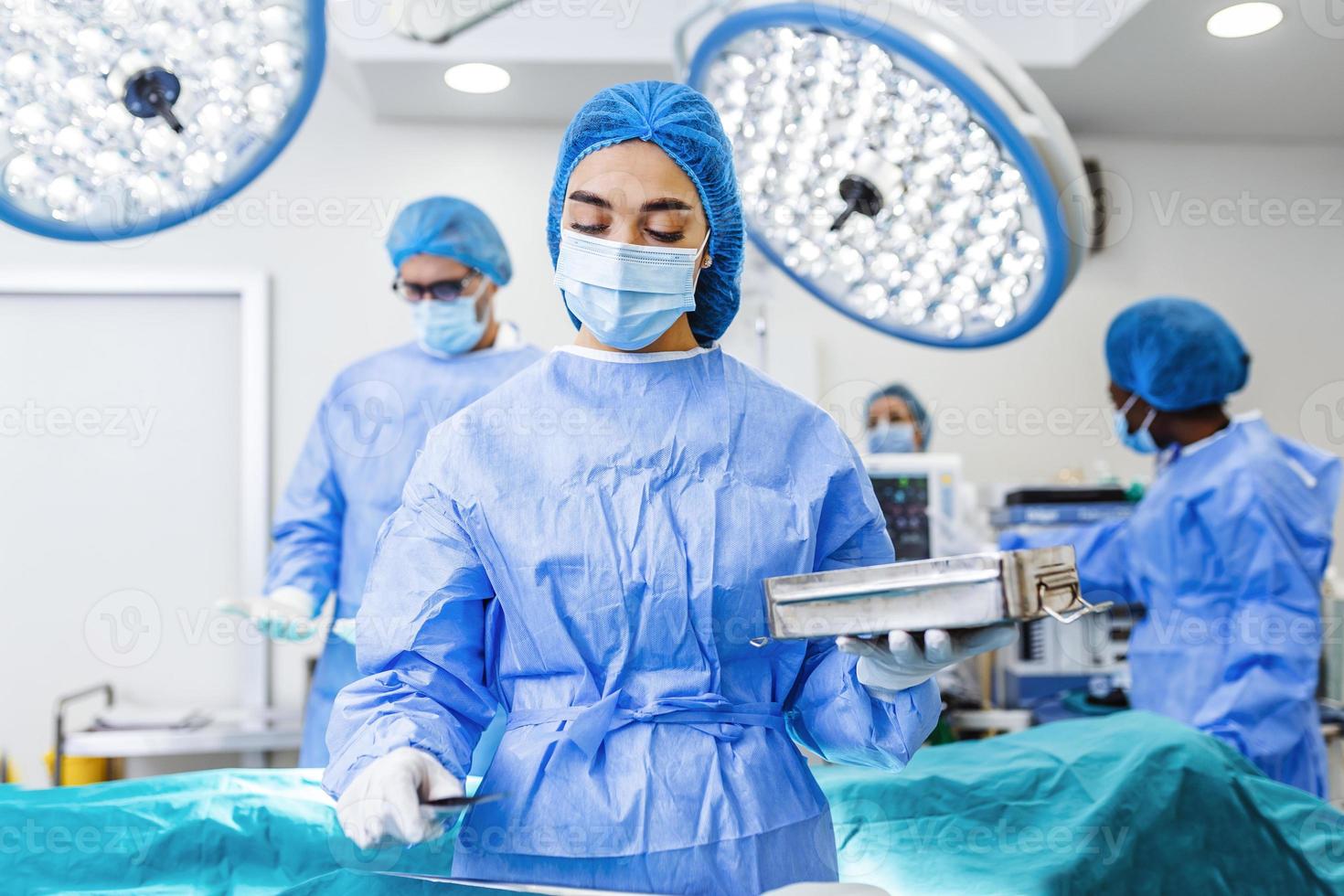 femmina chirurgo nel chirurgico uniforme assunzione chirurgico strumenti a operativo camera. giovane donna medico nel ospedale operazione Teatro foto