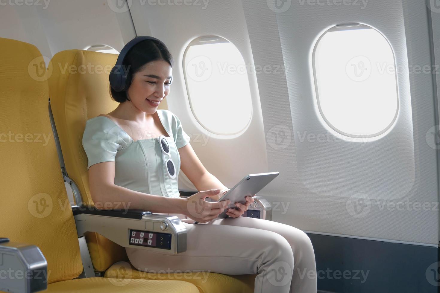 giovane femmina ascoltando preferito canzoni durante volo nel primo classe cabina utilizzando mobile elenco di riproduzione e accessorio, donna divertente su aereo tavola godendo musica nel cuffie a partire dal smartphone foto