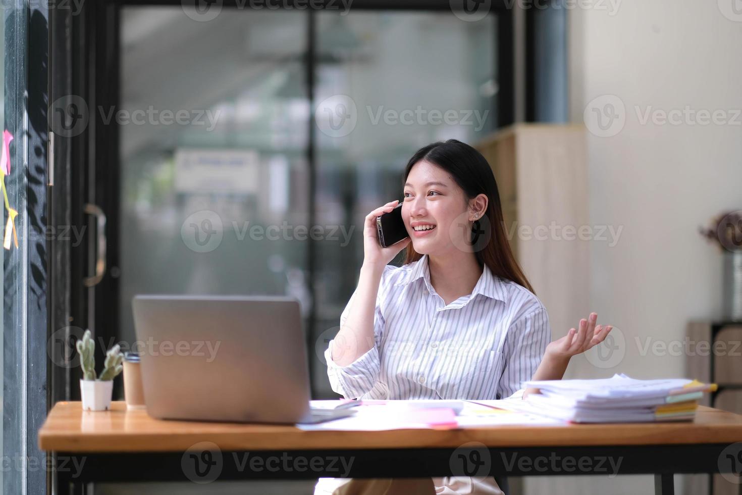 ritratto di giovane donna asiatica d'affari parlare su smartphone scrivere notebook portatile in ufficio a casa. bella ragazza al computer da scrivania portare a casa l'ordine. startup business asia donna online sme telemarketing. foto