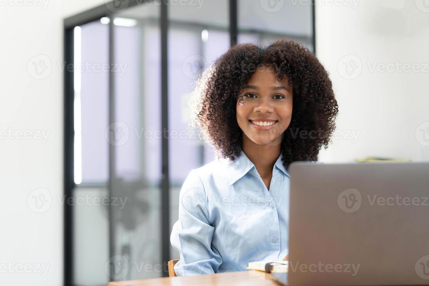 sorridente giovane africano femmina imprenditore seduta a un' scrivania nel sua casa ufficio Lavorando in linea con un' il computer portatile foto