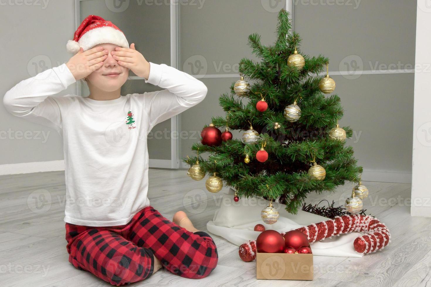 ragazza nel pigiama e un' Santa cappello si siede di il Natale albero con sua occhi Chiuso, Natale soddisfare foto