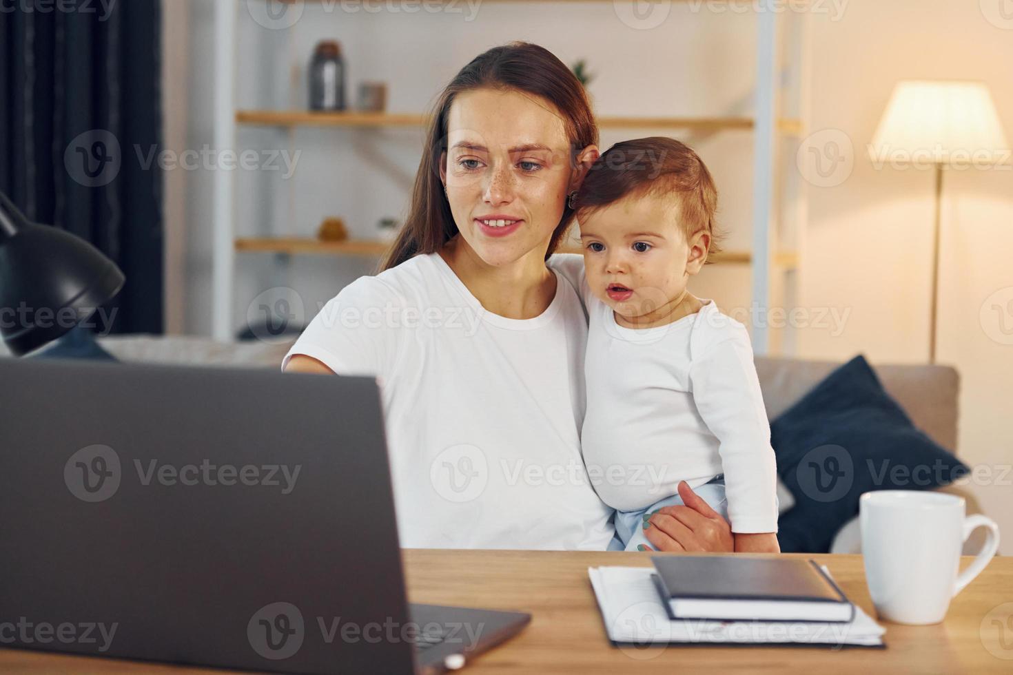 seduta di il tavolo con il computer portatile. madre con sua poco figlia è a casa insieme foto