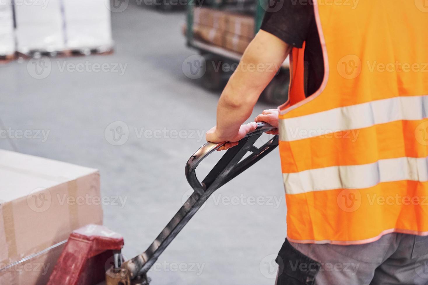 giovane maschio lavoratore nel uniforme è nel il magazzino spingendo pallet camion foto