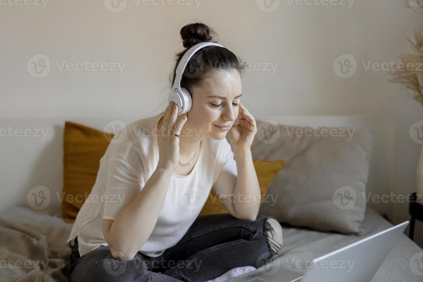 giovane brunetta donna seduta su il letto a casa con casuale Abiti e ascoltando musica o Audio libro. rilassante, riposo. tempo con te stesso, mentale Salute. ragazza sognando. foto