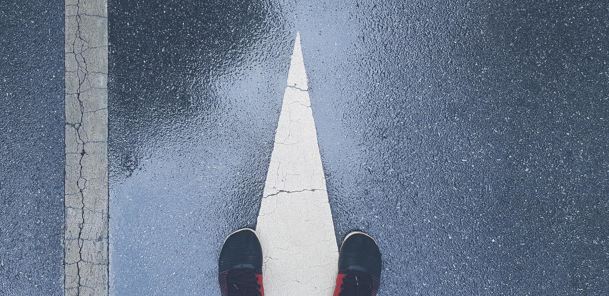 superiore Visualizza o piatto posare di sneaker o in esecuzione scarpe su bagnato strada o strada con bianca fine di direzione cartello e linea con copia spazio. scherzando e esercizio dopo pioggia nel Vintage ▾ tono. foto