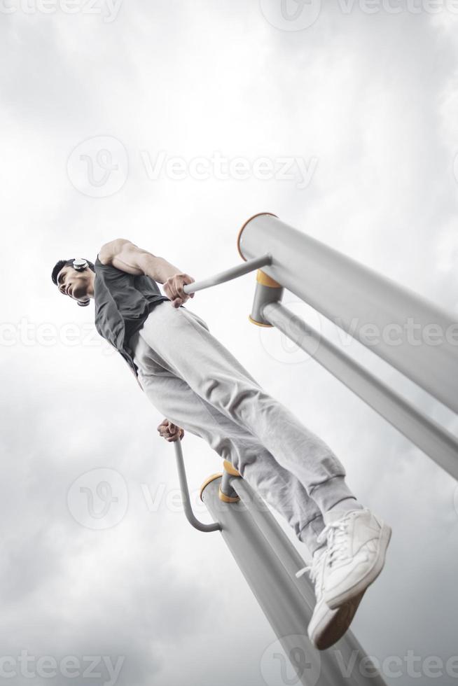 sportivo Lavorando su su il gli sport pubblico attrezzatura nel il all'aperto palestra. un' allegro attivo uomo nel un' parco a nuvoloso giorno. foto