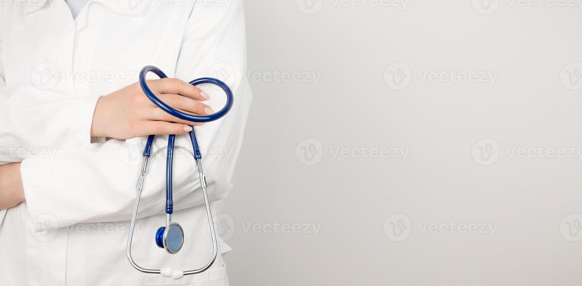 un' medico nel un' bianca medico cappotto detiene un' stetoscopio nel il suo mani. assistenza sanitaria concetto. bandiera con posto per testo foto