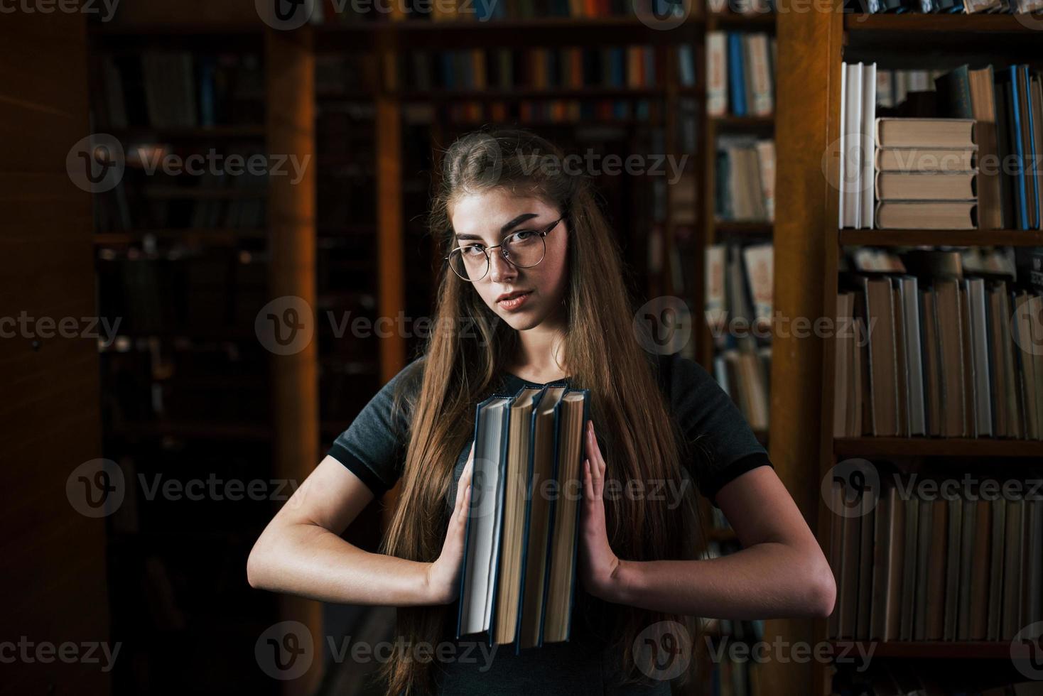 detiene molti libri nel mani. femmina alunno è nel biblioteca. concezione di formazione scolastica foto