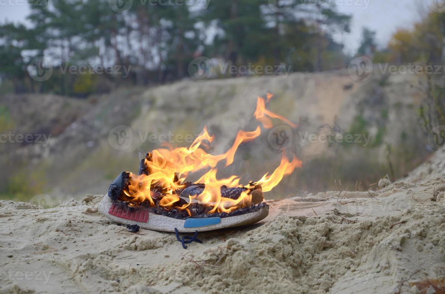 ardente gli sport scarpe da ginnastica o Palestra scarpe su fuoco In piedi su sabbioso spiaggia costa. atleta bruciato fuori. fisico sforzo durante formazione concetto foto