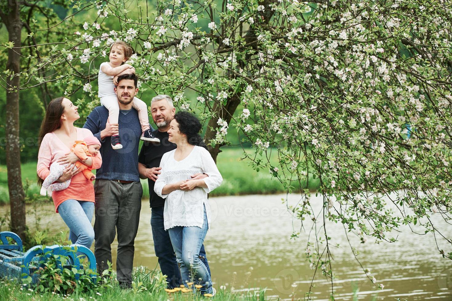 vicino alla panchina e al lago. foto di famiglia. ritratto a figura intera di persone allegre in piedi insieme all'aperto