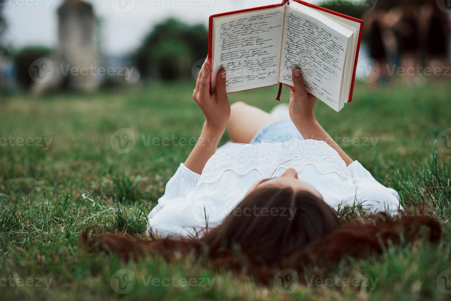 libro con rosso coperchio. ragazza dire bugie giù su il verde erba e avere un' riposo foto