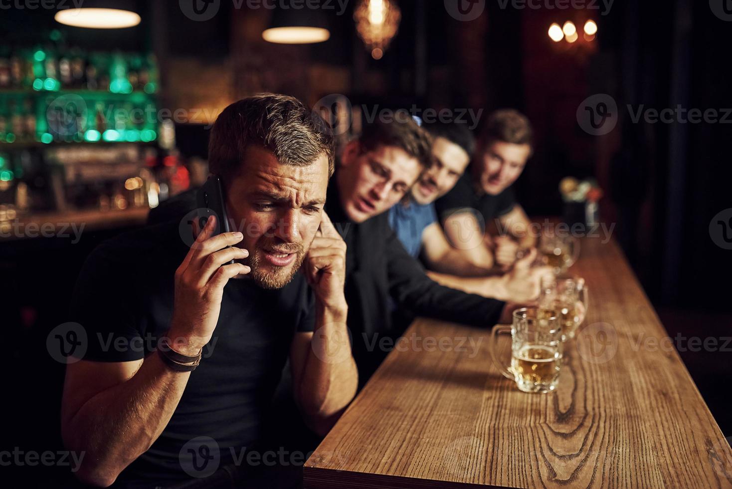 uomo parla di il Telefono. tre gli sport fan nel un' bar Guardando calcio. con birra nel mani foto