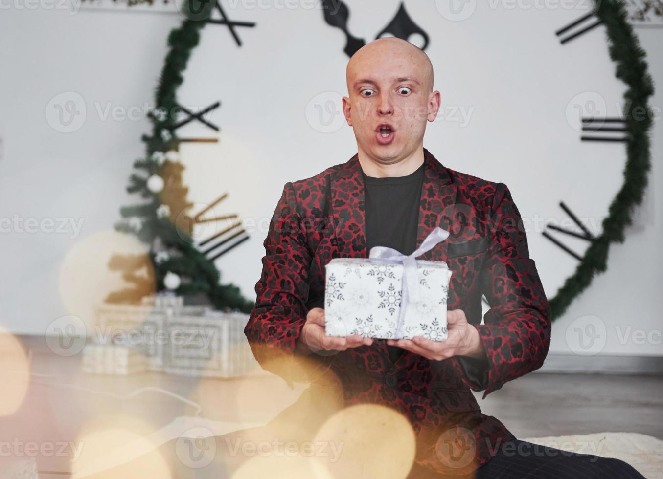 viso espressione. uomo con grande orologio dietro a lui seduta con nuovo anno regalo scatole nel vacanza vestiti foto