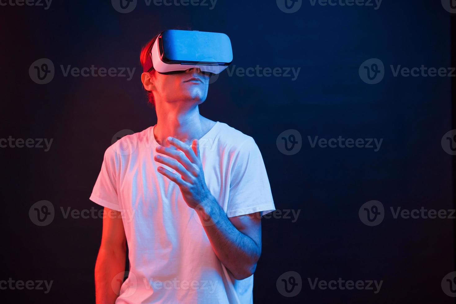 guardare su. giovane uomo utilizzando virtuale la realtà bicchieri nel il buio camera con neon illuminazione foto