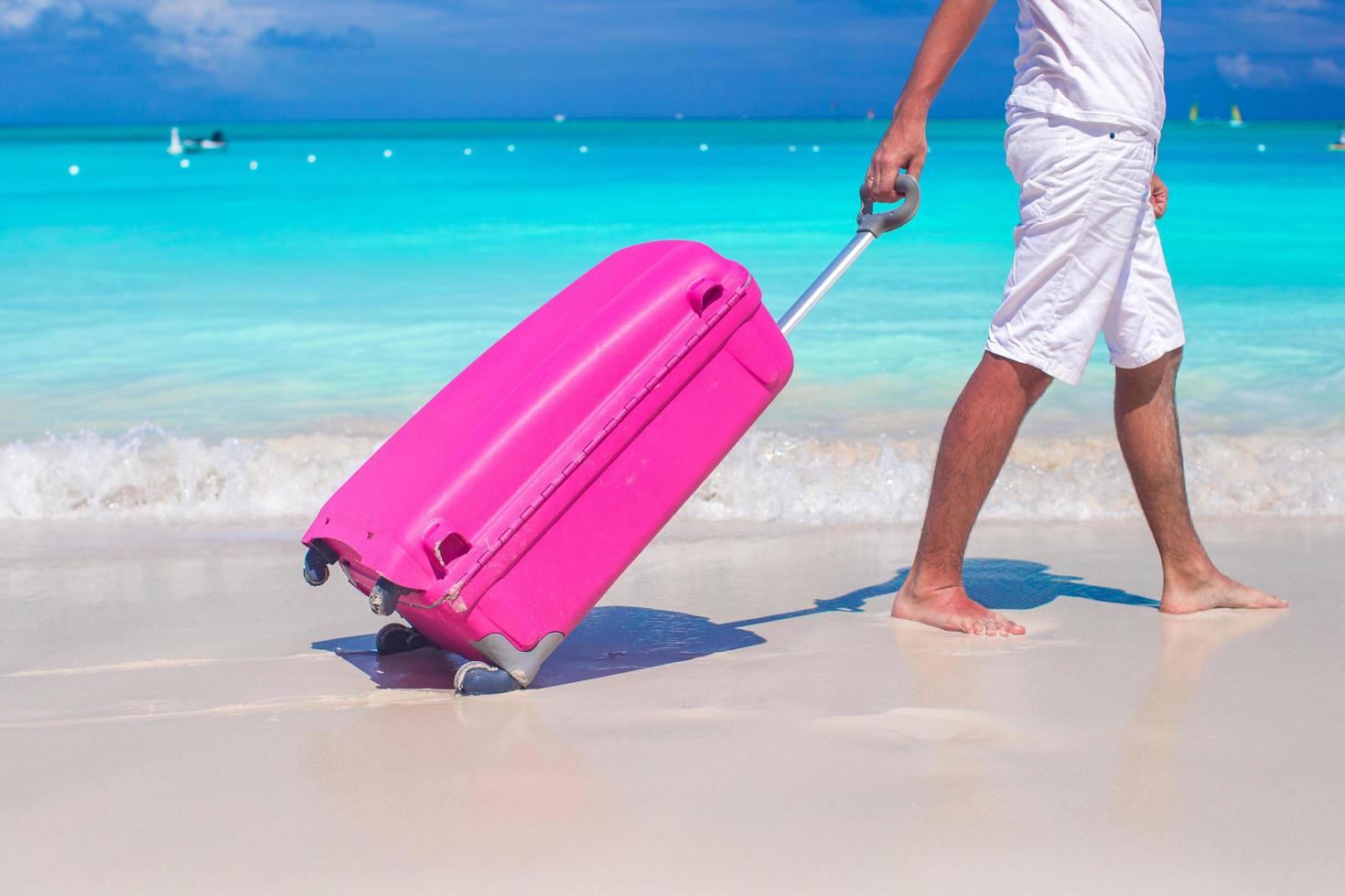 da vicino un uomo tira i bagagli sulla sabbia bianca foto
