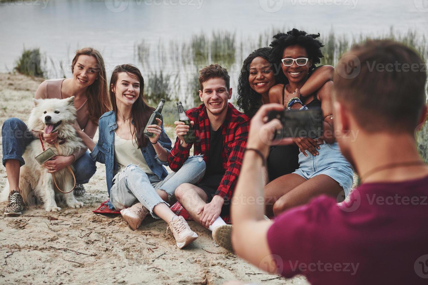 io volontà prendere foto di voi nel un' secondo. gruppo di persone avere picnic su il spiaggia. amici avere divertimento a fine settimana tempo