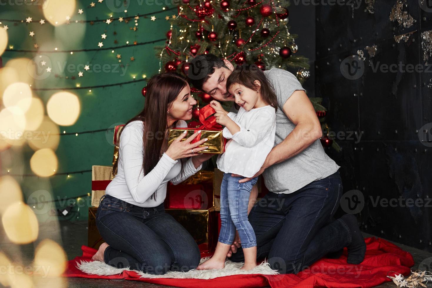 apertura il regalo. è quello è che cosa io pensare. bello famiglia si siede vicino il Natale albero con regalo scatole su inverno sera, godendo il tempo la spesa insieme foto