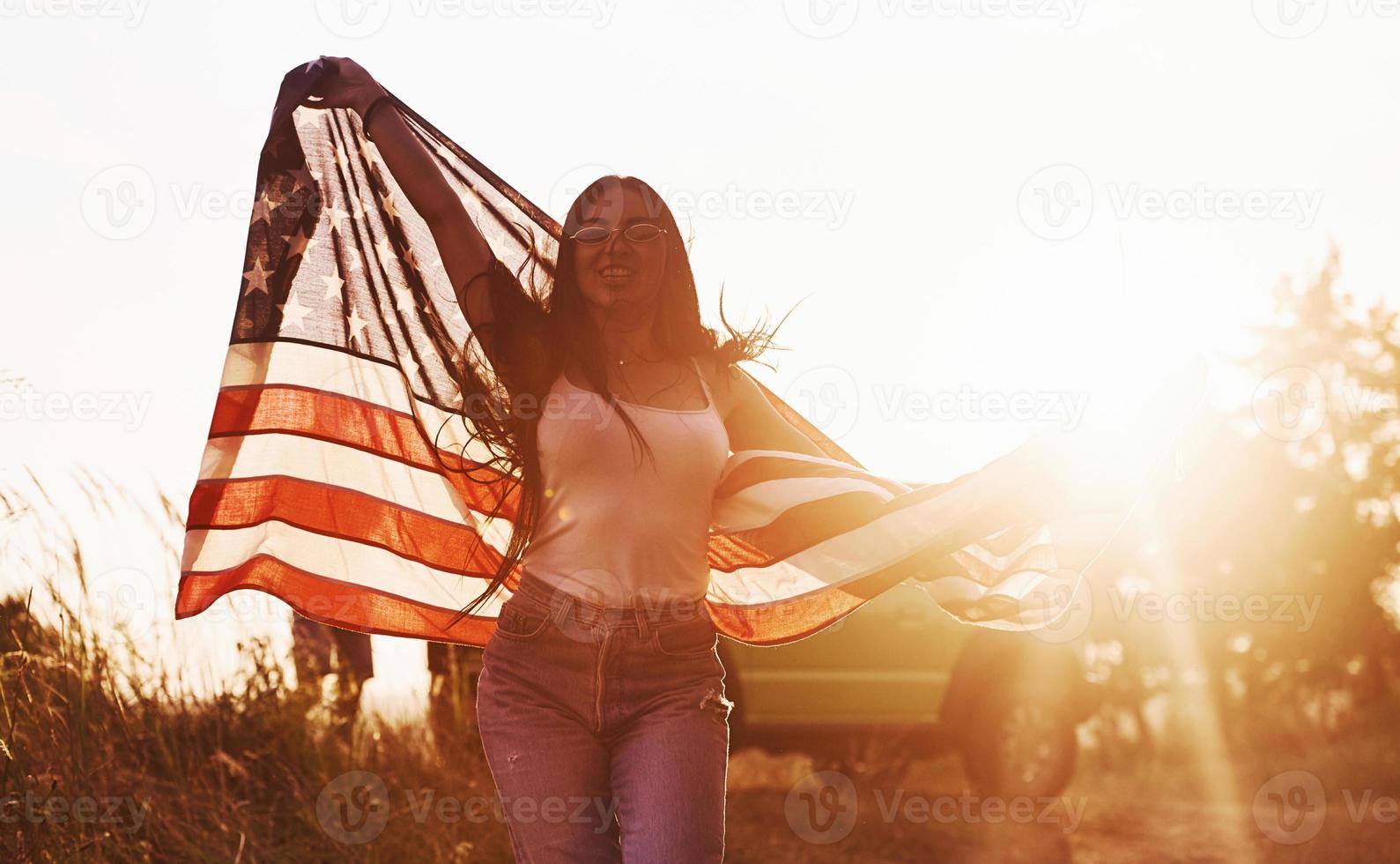 bellissimo luce. brunetta con Stati Uniti d'America bandiera nel mani avere un' bene tempo e si sente la libertà all'aperto a soleggiato giorno foto