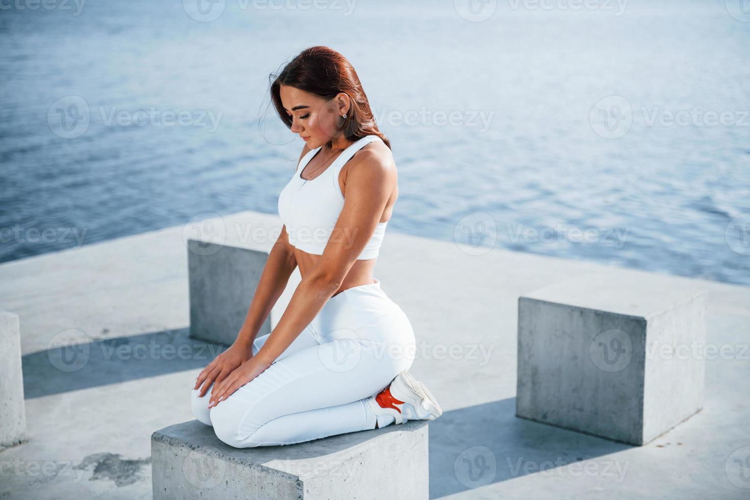 si siede su cemento cubo. fitness donna avendo un' riposo vicino il lago a giorno. bellissimo luce del sole foto