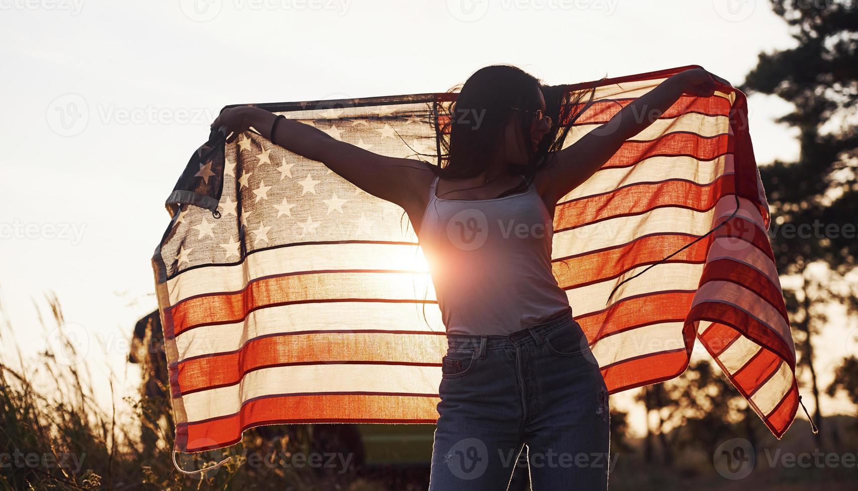 bellissimo luce. brunetta con Stati Uniti d'America bandiera nel mani avere un' bene tempo e si sente la libertà all'aperto a soleggiato giorno foto