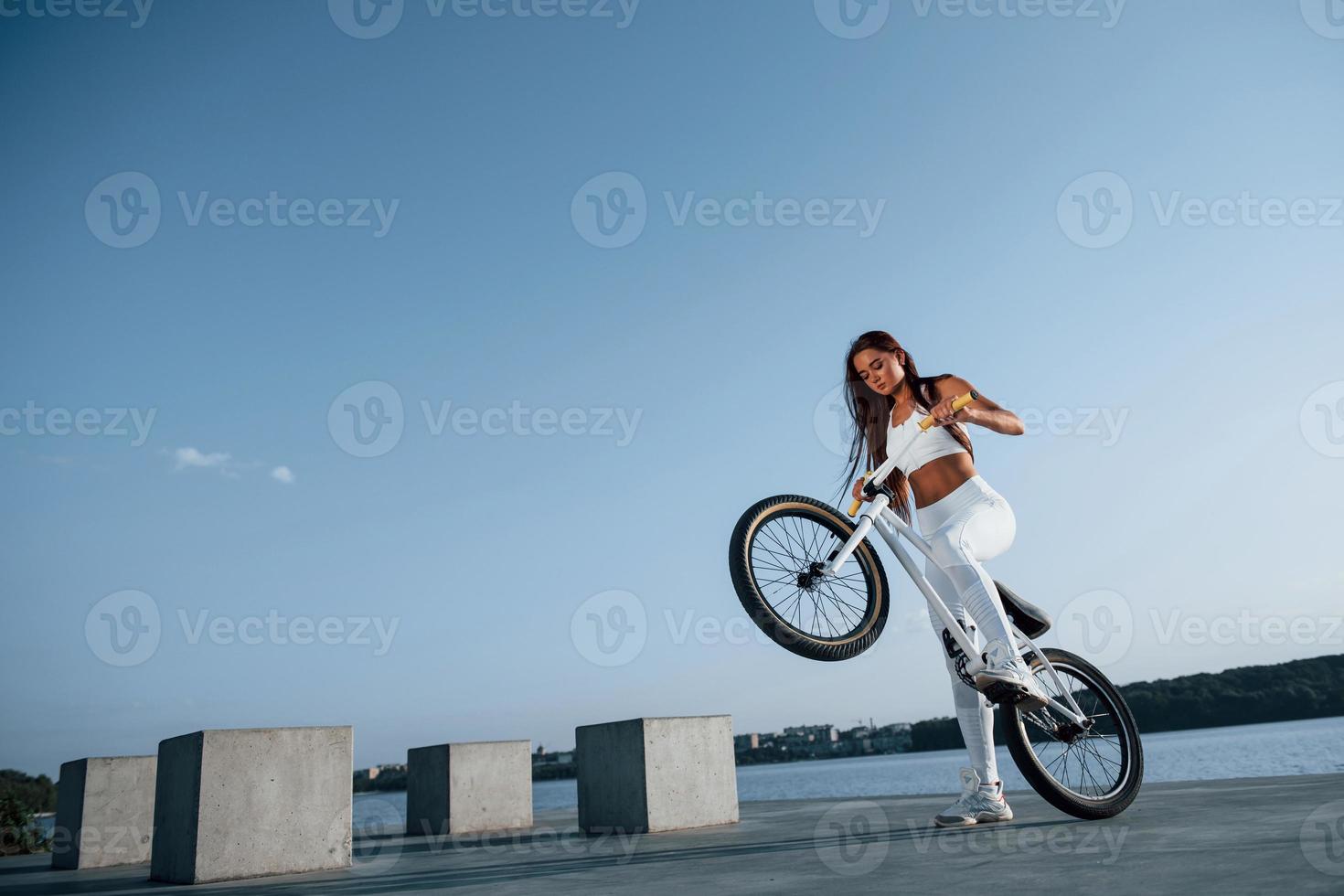 foto nel movimento. fare acrobazie. femmina ciclista è su il bicicletta a giorno vicino il lago. fitness donna nel allegro Abiti