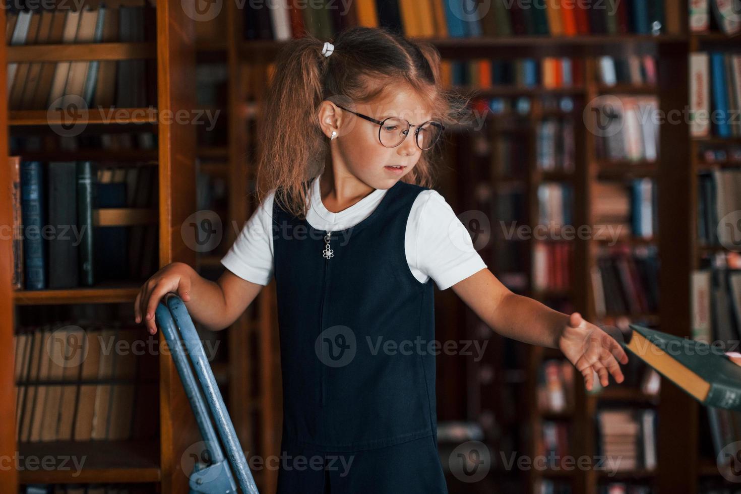 scuola ragazza su il scala nel biblioteca pieno di libri. formazione scolastica concezione foto