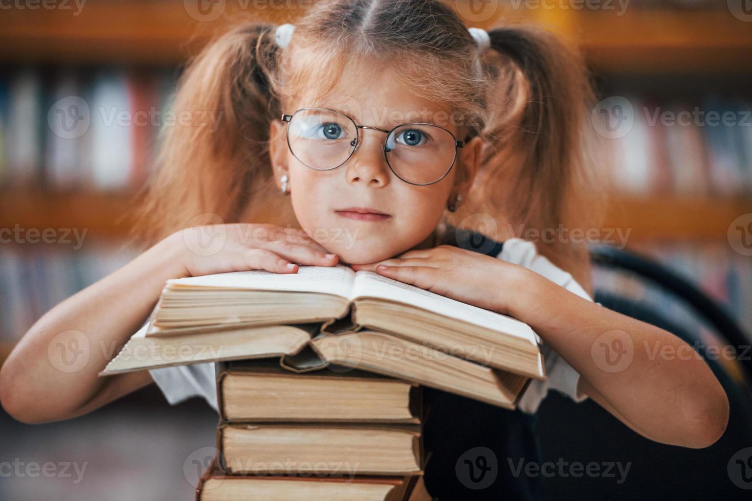 pendente su il libri. carino poco ragazza con trecce è nel il biblioteca foto