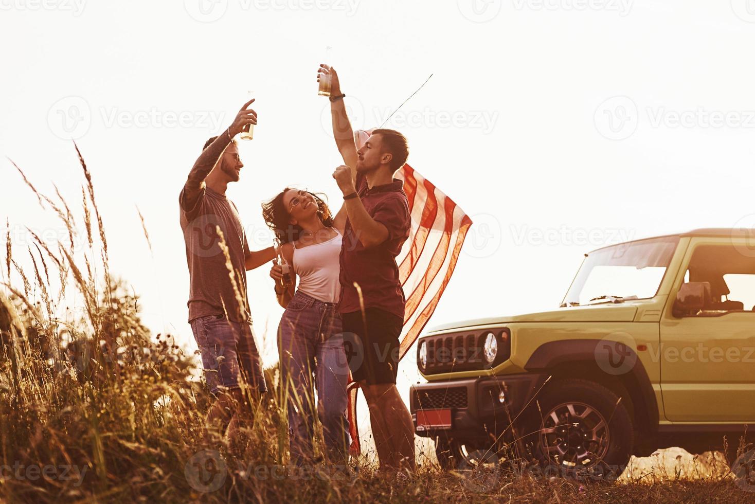 dando Saluti. amici avere simpatico fine settimana all'aperto vicino il loro verde auto con Stati Uniti d'America bandiera foto
