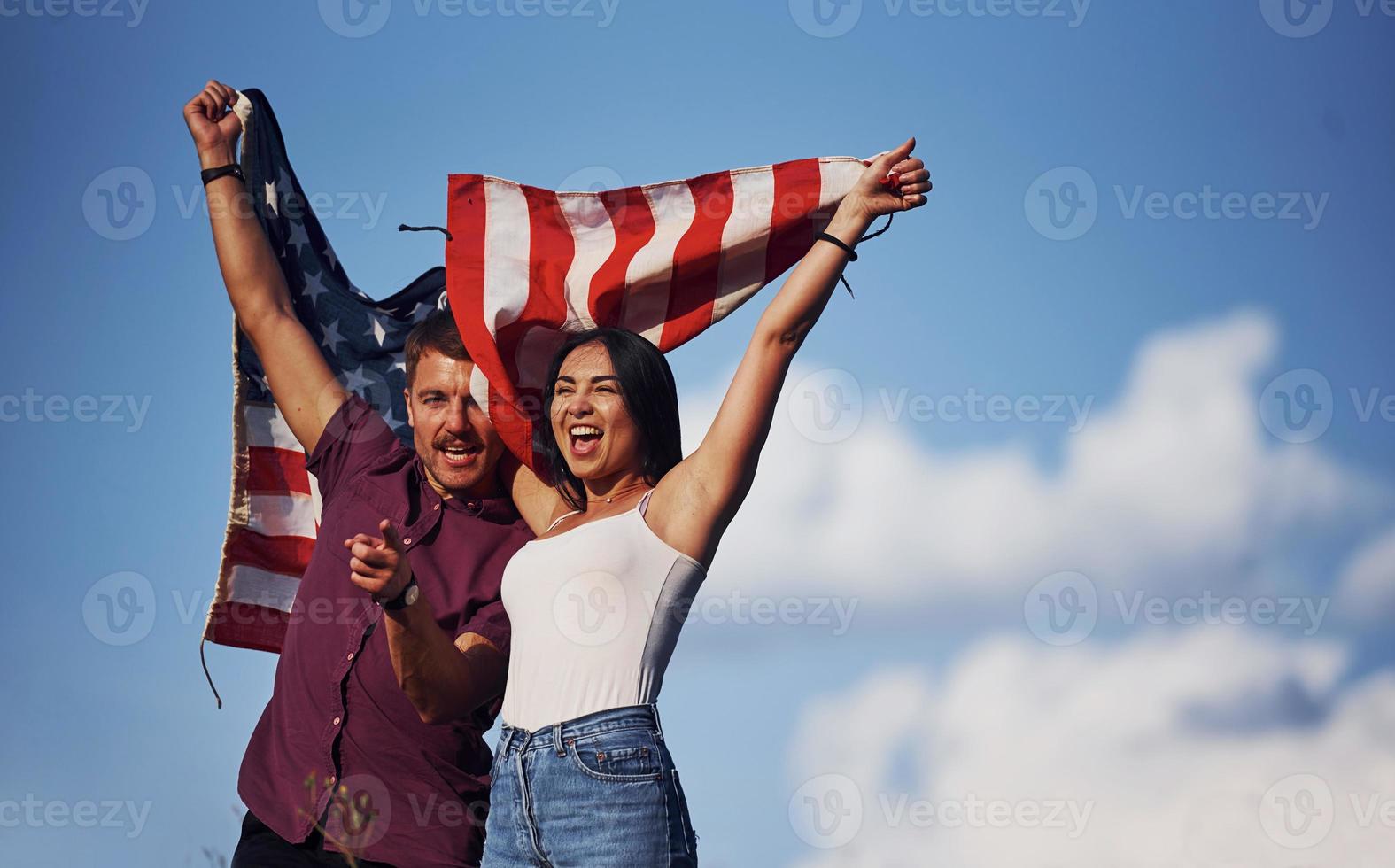 con mani su. si sente libertà. bellissimo coppia con americano bandiera avere un' bene tempo all'aperto nel il campo foto