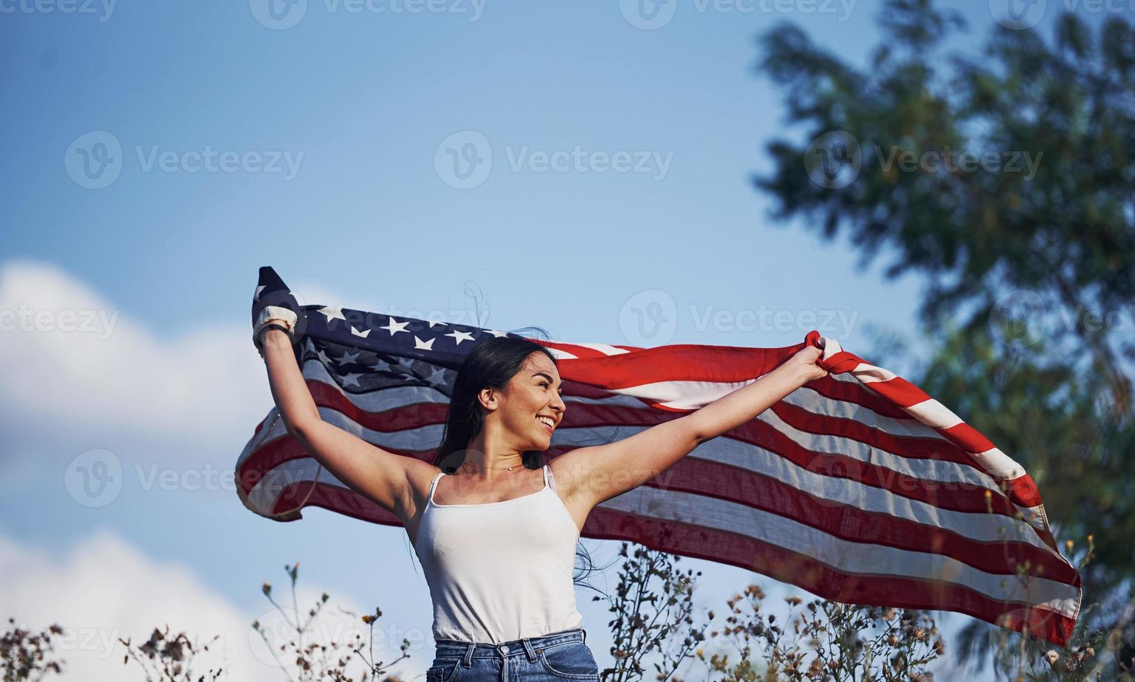 femmina patriota corre con Stati Uniti d'America bandiera nel mani all'aperto nel il campo contro blu cielo foto