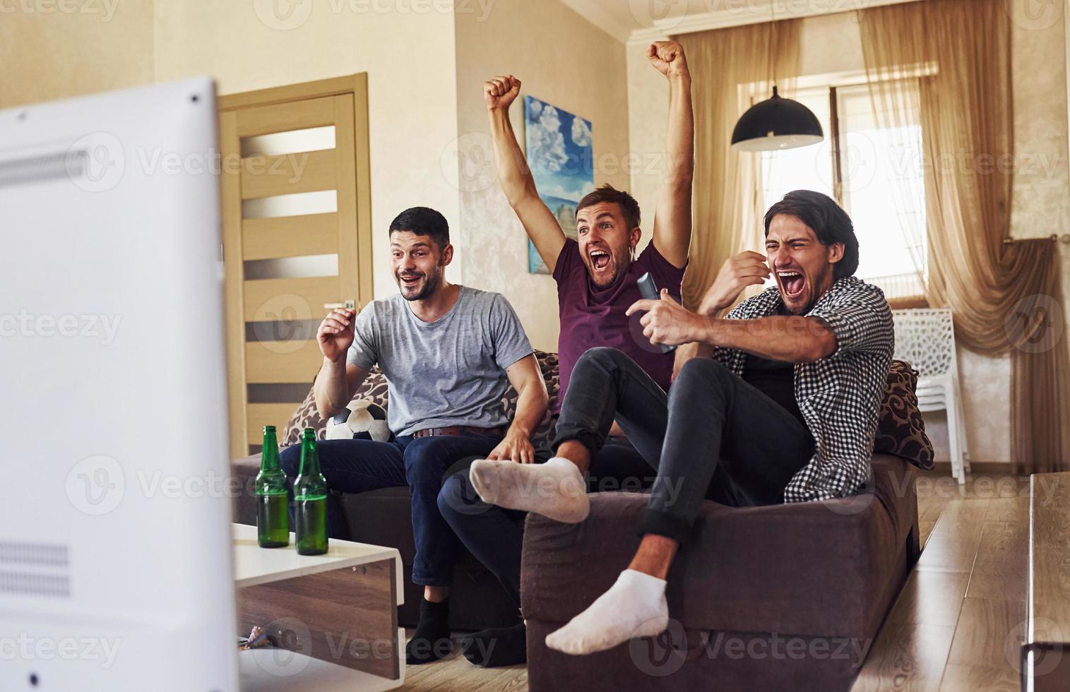 festeggiare vittoria. eccitato tre amici Guardando calcio su tv a casa insieme foto