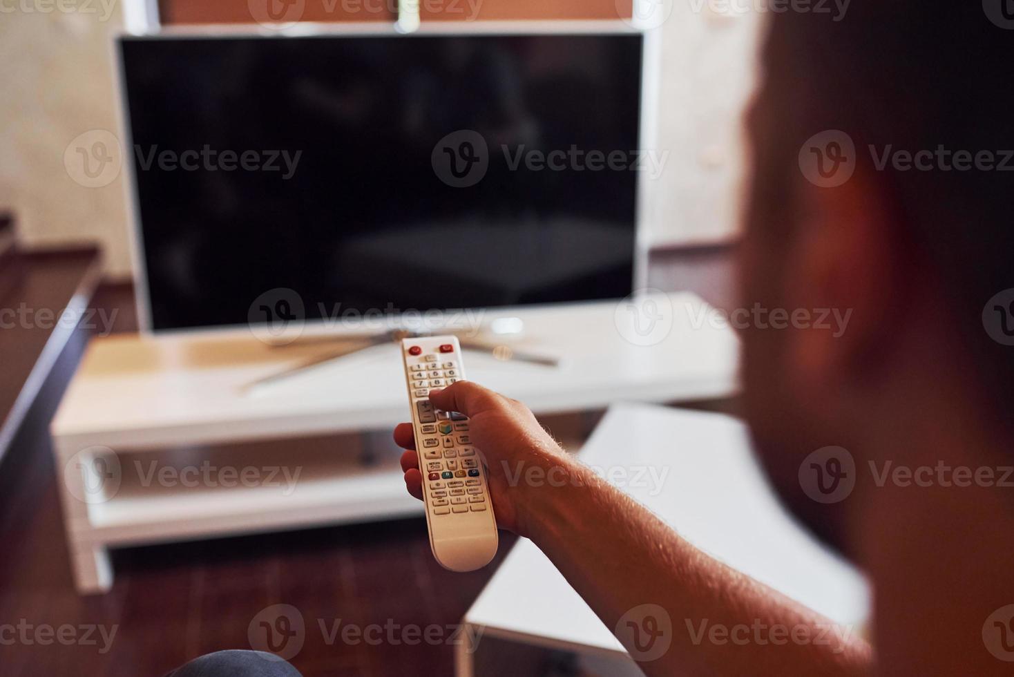 sostegno Visualizza di uomo detiene a distanza controllore nel mano e svolta su tv foto