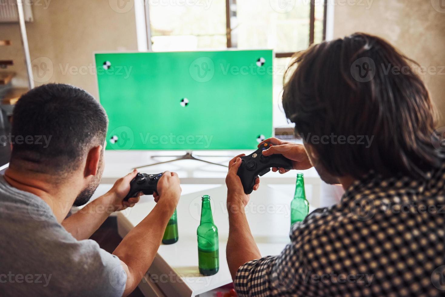 birra su il tavolo. gruppo di amici avere divertimento giocando consolle gioco in casa a vivente camera foto