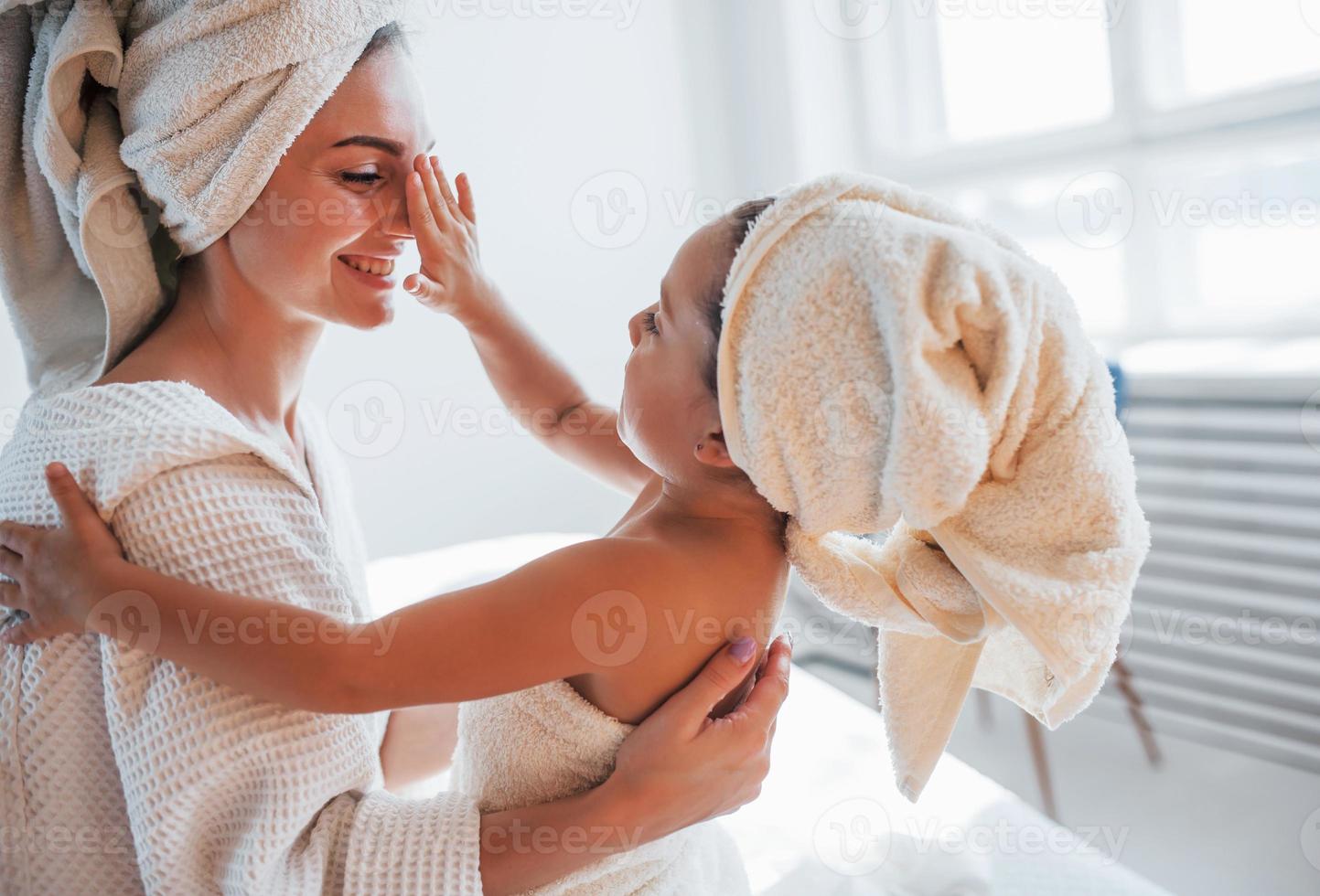 giocoso umore. giovane madre con sua figlia avere bellezza giorno in casa nel bianca camera foto