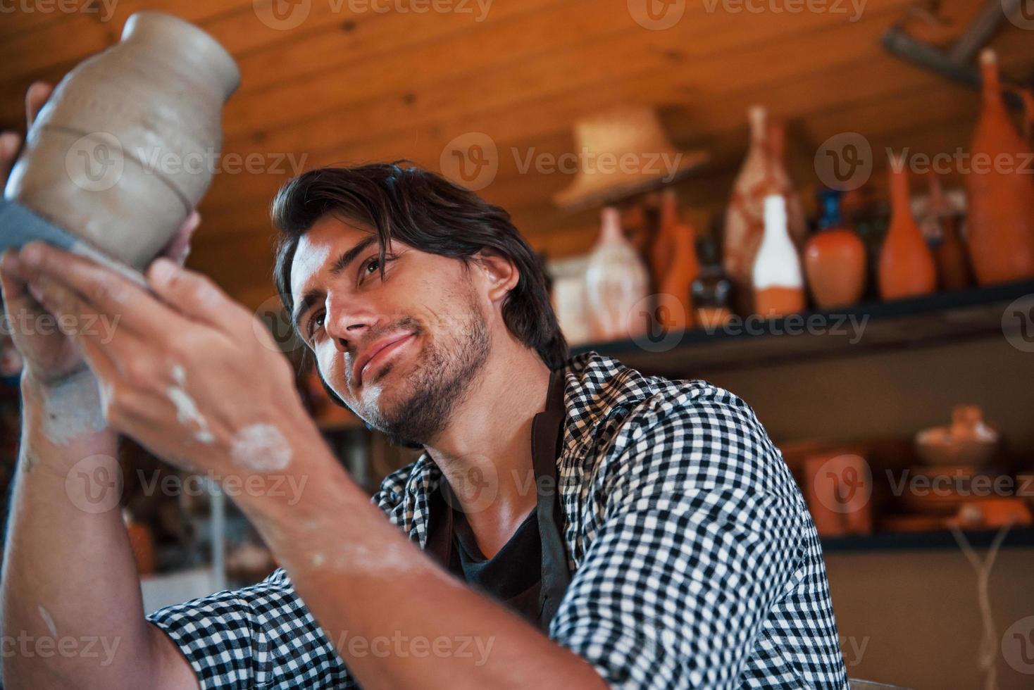 giovane ceramista detiene fresco fatto a mano pentola nel mano e sembra a risultati di il suo opera foto