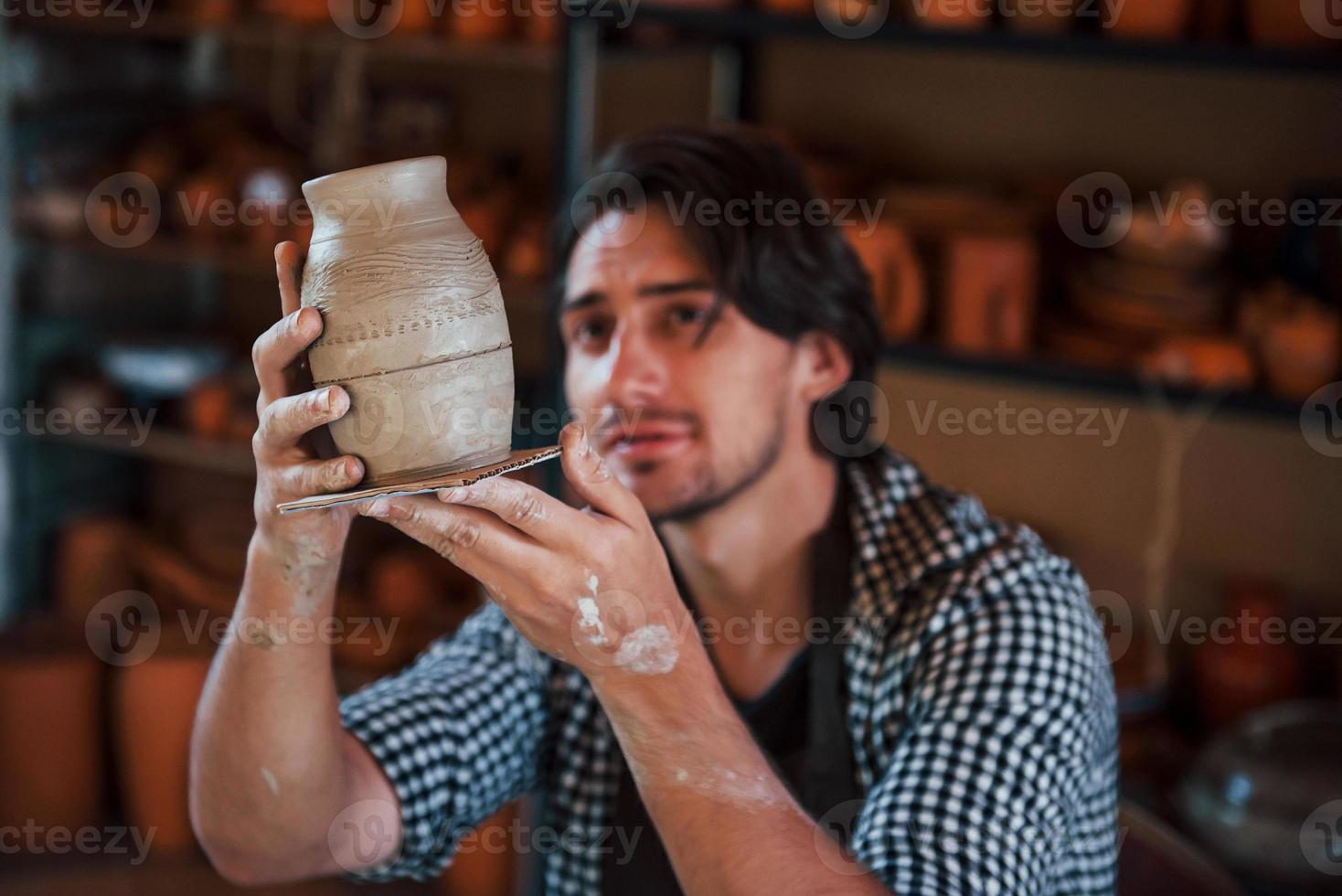 giovane ceramista detiene fresco fatto a mano pentola nel mano e sembra a risultati di il suo opera foto