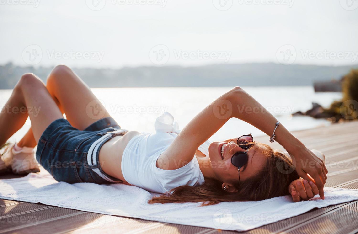 ragazza vicino il lago dire bugie giù su il terra e godendo caldo luce del sole foto