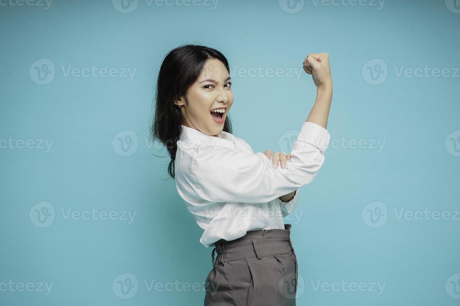 eccitato asiatico donna indossare un' bianca camicia mostrando forte gesto di sollevamento sua braccia e muscoli sorridente con orgoglio foto