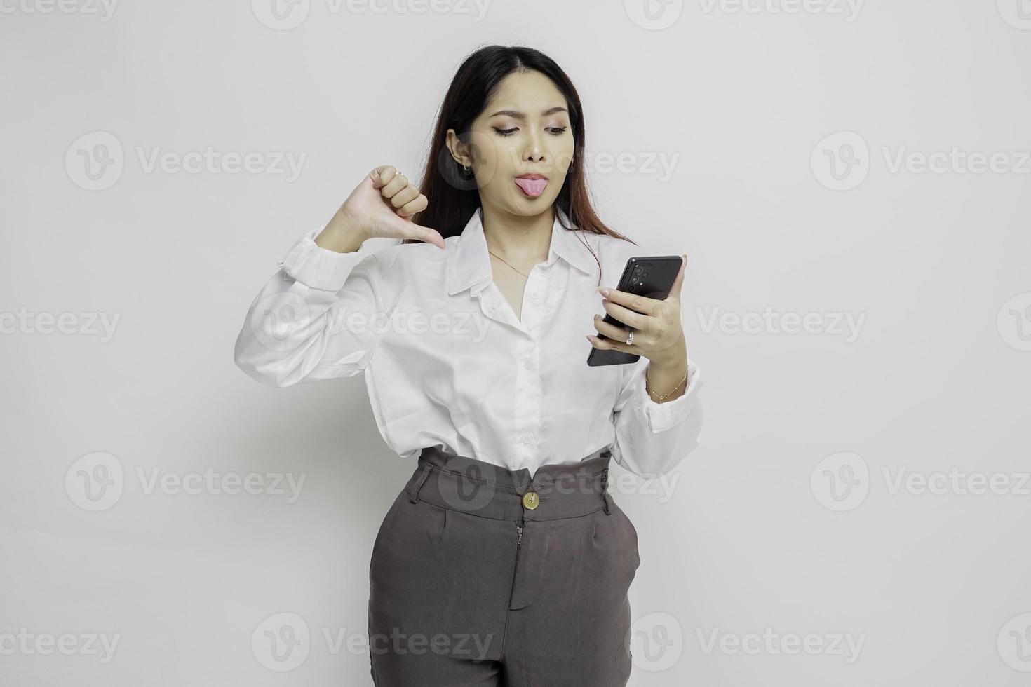 un' deluso asiatico donna indossare bianca camicia dà pollici giù mano gesto di disapprovazione, isolato di bianca sfondo foto