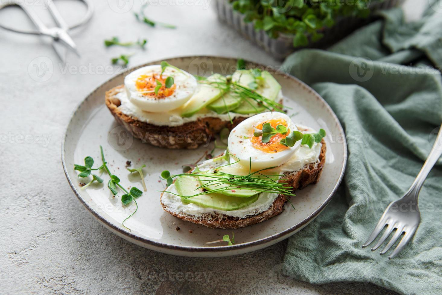 pane tostato, uova sode, fetta di avocado, microgreens su un piatto foto