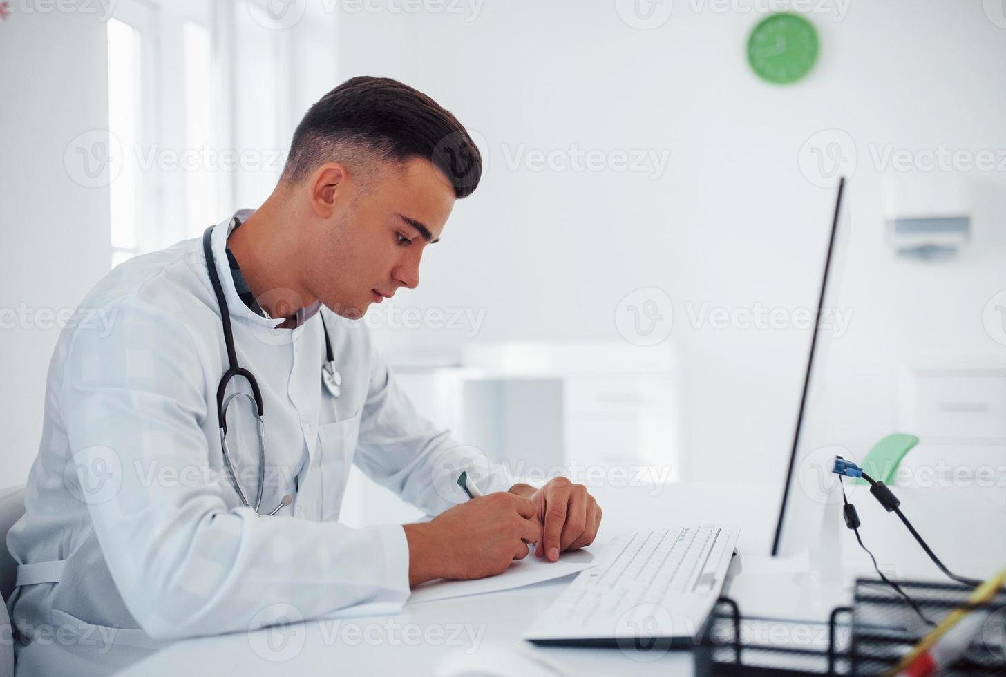 Lavorando con documenti. giovane elegante maschio medico con stetoscopio è nel clinica a giorno foto