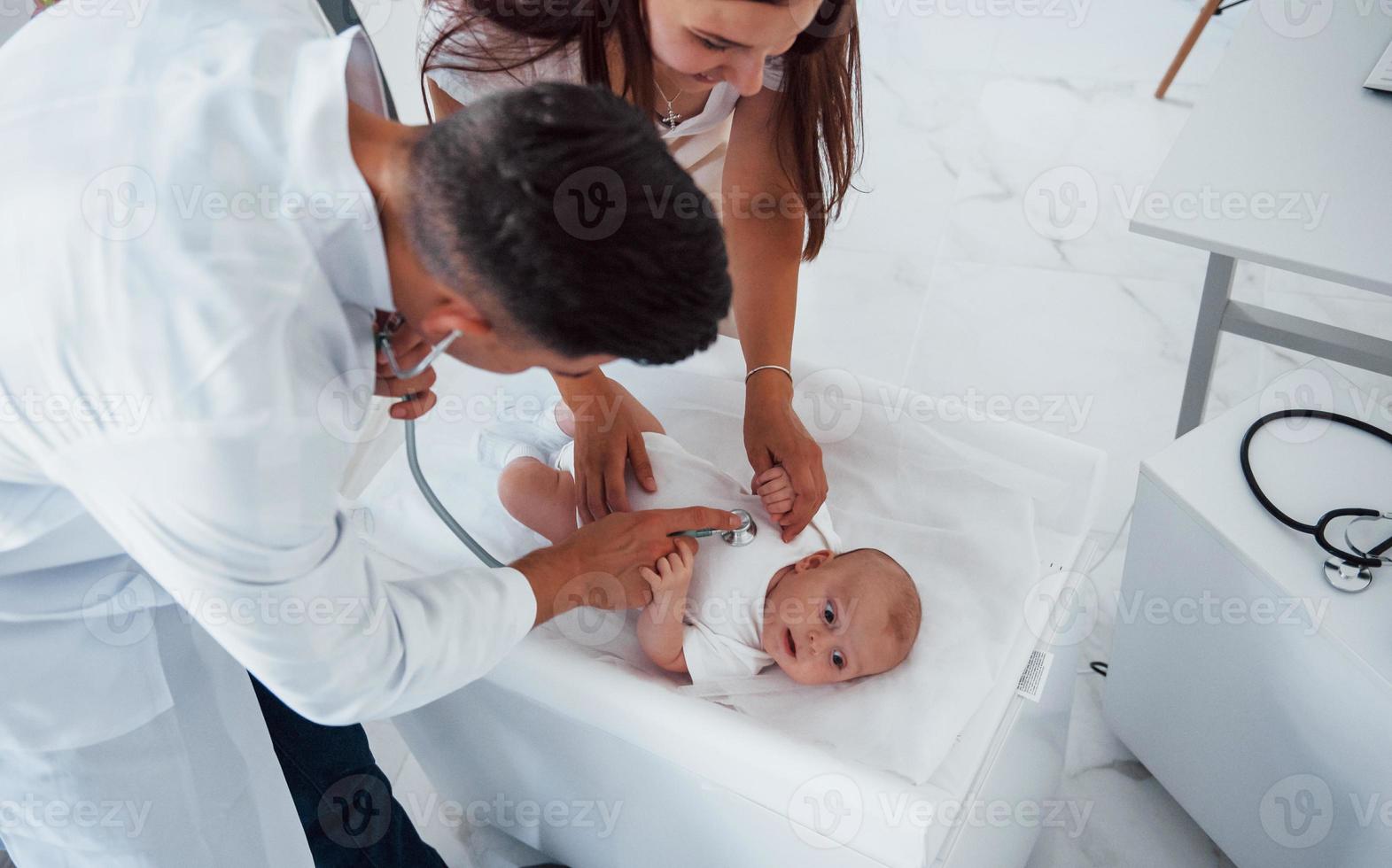 giovane pediatra è con poco bambino nel il clinica a giorno foto