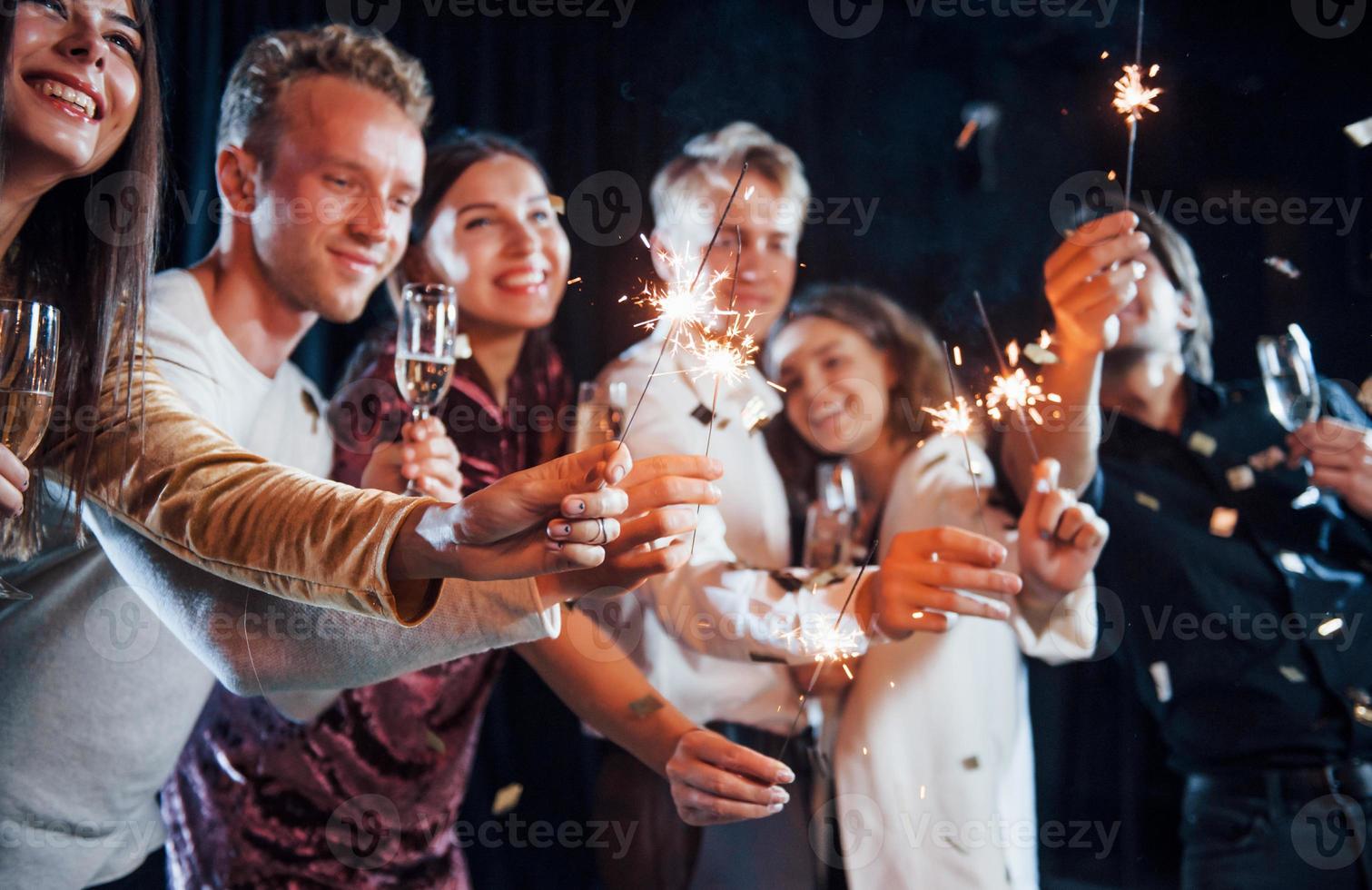 avendo divertimento con spumanti. coriandoli è nel il aria. gruppo di allegro amici festeggiare nuovo anno in casa con bevande nel mani foto