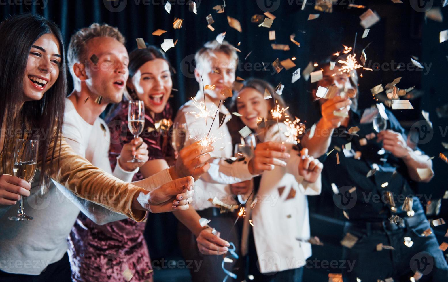 avendo divertimento con spumanti. coriandoli è nel il aria. gruppo di allegro amici festeggiare nuovo anno in casa con bevande nel mani foto